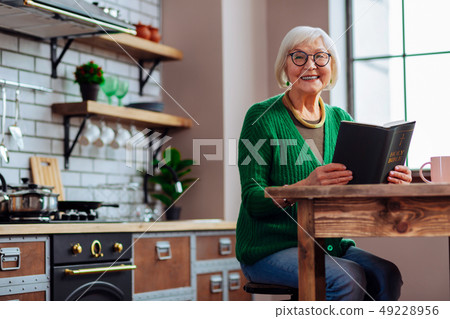 Smiling female happily keeping book in hands at kitchen room 49228956