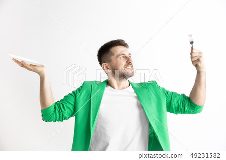 Young smiling attractive guy holding empty dish and fork isolated on grey background. Young smiling attractive guy holding empty dish and fork isolated on grey background. 49231582