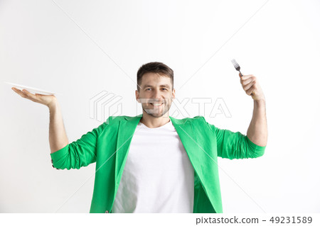 Young smiling attractive guy holding empty dish and fork isolated on grey background. Young smiling attractive guy holding empty dish and fork isolated on grey background. 49231589