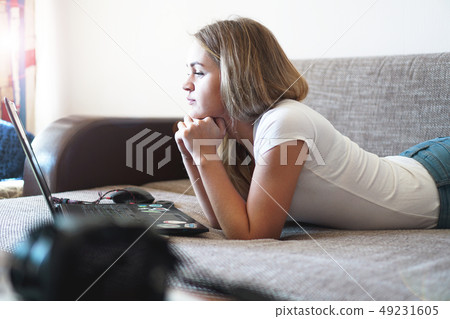 Young woman relaxing with a laptop in her living room Young woman relaxing with a laptop in her living room 49231605