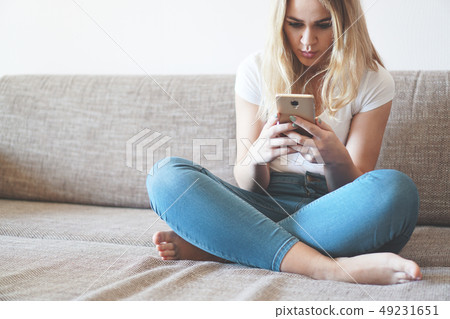 Attractive young woman relaxing on a sofa at home and using smart phone Attractive young woman relaxing on a sofa at home and using smart phone 49231651