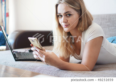 Attractive young woman relaxing on a sofa at home and using smart phone Attractive young woman relaxing on a sofa at home and using smart phone 49231659