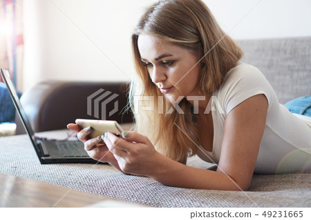 Attractive young woman relaxing on a sofa at home and using smart phone Attractive young woman relaxing on a sofa at home and using smart phone 49231665