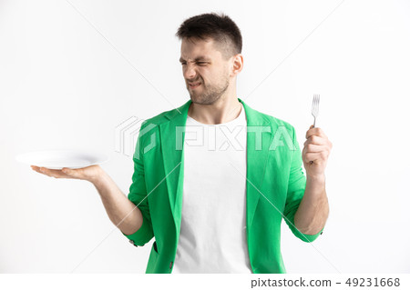Young sad attractive guy holding empty dish and fork isolated on grey background. 49231668