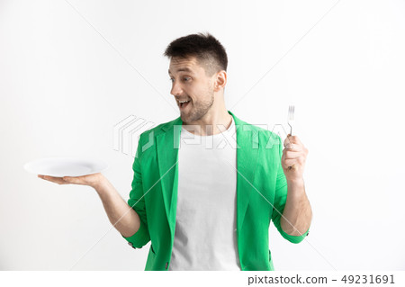 Young smiling attractive guy holding empty dish and fork isolated on grey background. Young smiling attractive guy holding empty dish and fork isolated on grey background. 49231691