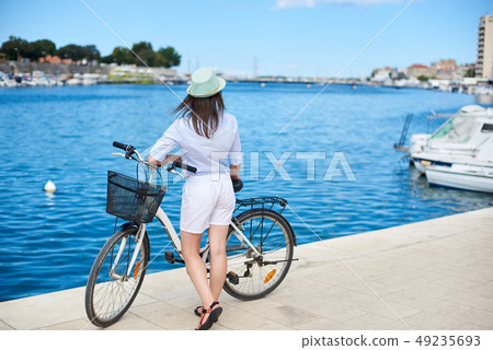 Young woman with backpack riding city bicycle near sea Young woman with backpack riding city bicycle near sea 49235693