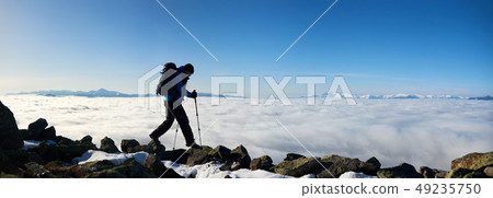 Hiker on rocky hill on background of valley with white clouds, snowy mountains and blue sky. 49235750