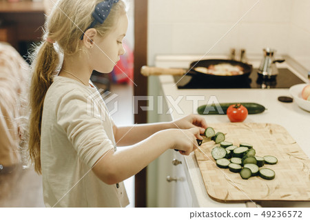 Little blonde girl cutting vegetables while cooking in kitchen at home 49236572