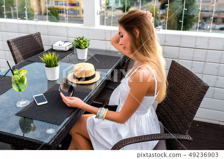A woman with long hair, beautiful girl sitting summer cafe. Watching movie tablet. Table telephone 49236903