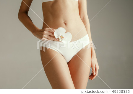 Young woman with epilated bikini zone holding flower on light background Young woman with epilated bikini zone holding flower on light background 49238525