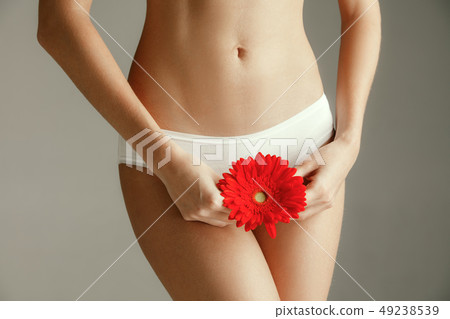 Young woman with epilated bikini zone holding flower on light background 49238539