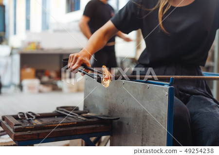 A glassblower student tries to make a flower out of glass A glassblower student tries to make a flower out of glass 49254238