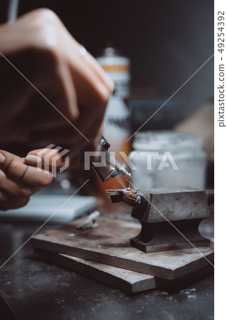 In the workshop, a woman jeweler is busy soldering jewelry In the workshop, a woman jeweler is busy soldering jewelry 49254392