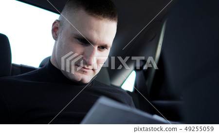 Businessman looking through documents while sitting at the back of a car Businessman looking through documents while sitting at the back of a car 49255059
