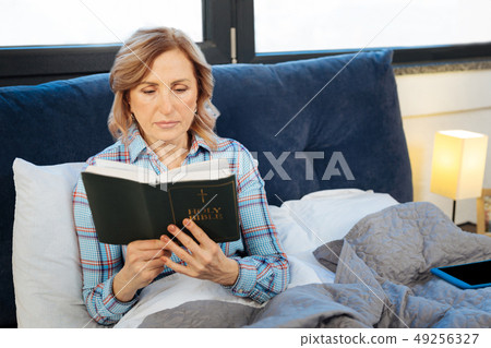 Positive calm woman holding open bible and thoughtfully reading 49256327