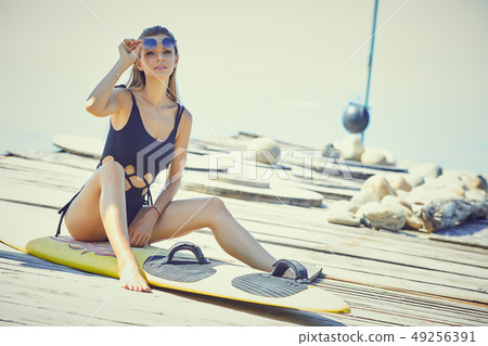 Young woman in wetsuit with surfing board standing 49256391