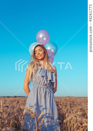 Happy girl smiling, beautiful woman stands in summer in a wheat field. Holds balloons in his hand 49261773