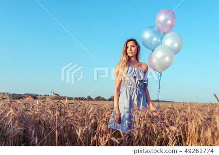 Beautiful girl stands in summer in a wheat field. In her hand a woman holds balloons. Rest after the 49261774