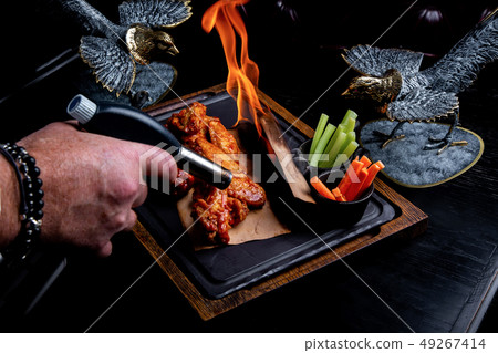 Delicious pieces of chicken wings grilled with Fire flames. On restaurant black background. Barbecue Delicious pieces of chicken wings grilled with Fire flames. On restaurant black background. Barbecue 49267414