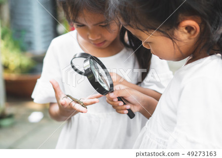 Two girls use magnifying glass look on grasshopper 49273163
