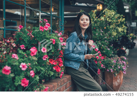 woman holding cellphone sitting by garden 49274155