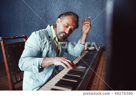 Handsome musician composes music sitting at piano Handsome musician composes music sitting at piano 49278380