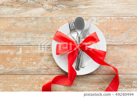 cutlery tied with red ribbon on set of plates 49280494