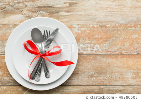 cutlery tied with red ribbon on set of plates 49280503