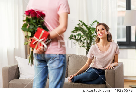 woman looking at man with flowers and gift at home woman looking at man with flowers and gift at home 49280572