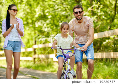 kid with patents learning to ride bicycle in park 49280717