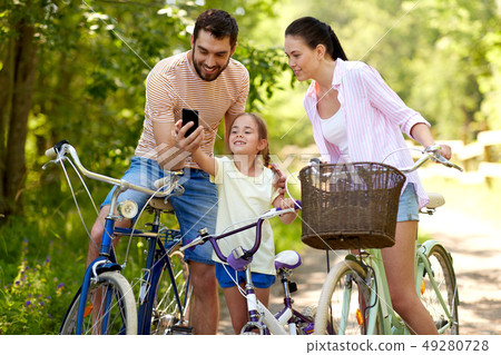 family with smartphone and bicycles in summer park family with smartphone and bicycles in summer park 49280728