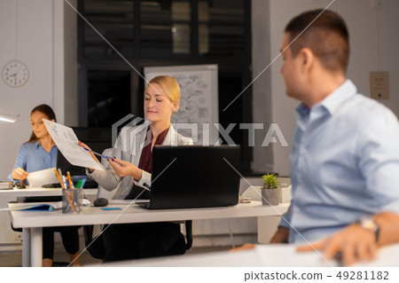 woman showing charths to colleague at night office 49281182