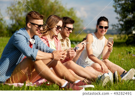smiling friends with smartphones sitting on grass smiling friends with smartphones sitting on grass 49282491