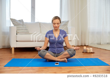 woman with music on smartphone meditating at home woman with music on smartphone meditating at home 49283518