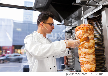 chef slicing doner meat from spit at kebab shop 49284049