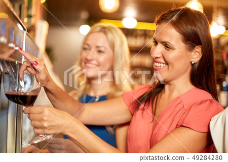 happy women pouring wine from dispenser at bar 49284280