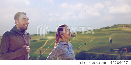 happy couple with earphones running outdoors 49284457