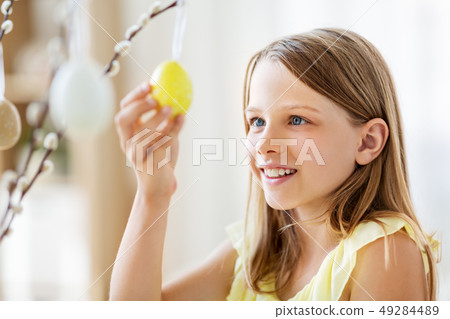 girl decorating willow by easter eggs at home 49284489