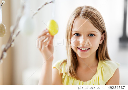girl decorating willow by easter eggs at home 49284587