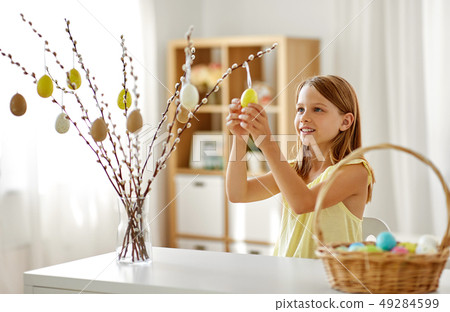 girl decorating willow by easter eggs at home 49284599