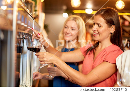 happy women pouring wine from dispenser at bar 49285740