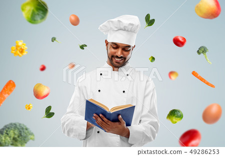 happy indian chef reading cookbook over vegetables 49286253