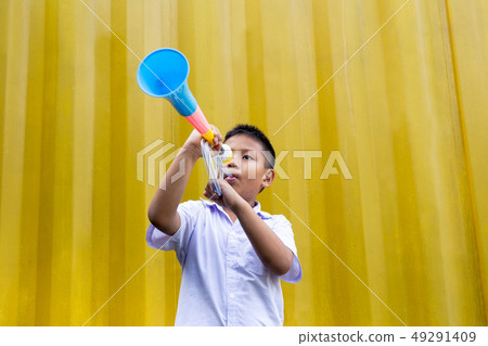 Asian school boy blowing a colorful horn in yellow background. 49291409