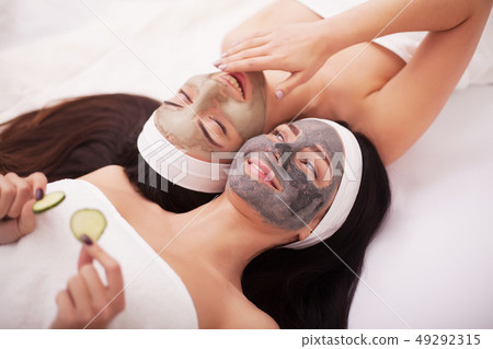Home spa. Two beautiful young women holding pieces of cucumber on their eyes and smiling while on 49292315