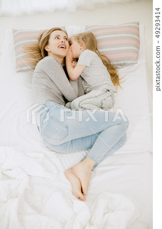 Young mother and her little daughter hugging and kissing on bed Young mother and her little daughter hugging and kissing on bed 49293414