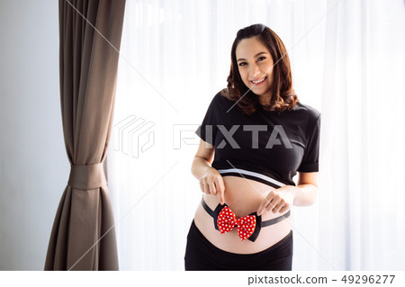 Pregnant woman holding  tummy with ribbon bow over window view 49296277