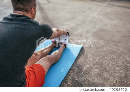 A male athlete doing gymnastics on mat, stretching muscles, training summer city on sports field 49298720
