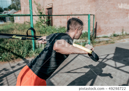 Male athlete, wrung out on loops, training straps, in summer in the city on the sports field. Active 49298722