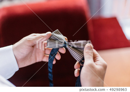 A man holds a stylish bow tie in his hands. 49298963