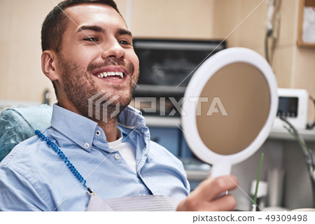Your smile is our mission. Handsome male patient looking at his beautiful smile sitting at the Your smile is our mission. Handsome male patient looking at his beautiful smile sitting at the 49309498